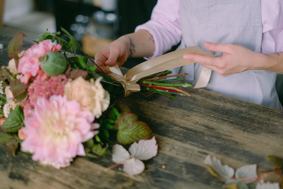 Fleuriste en train de nouer un ruban autour d'un bouquet de fleurs sur une table en bois.