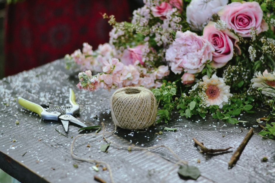 Matériel de création de centre de table avec des fleurs, des ciseaux de jardinage et une pelote de ficelle sur une table en b