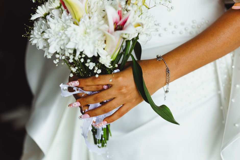 Femme en robe de mariée tenant un bouquet de fleurs blanches et roses avec des détails délicats.
