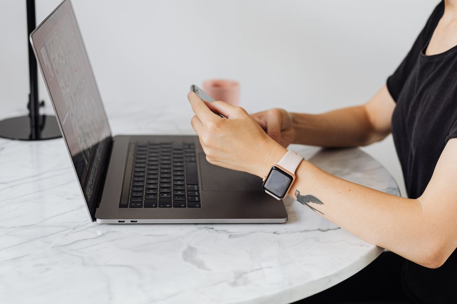 Personne utilisant un smartphone tout en travaillant sur un ordinateur portable sur une table en marbre.