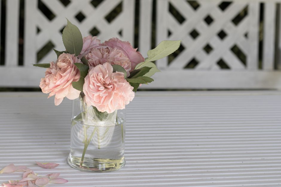Bouquet de roses roses dans un vase transparent sur une table blanche, pétales éparpillés à côté.