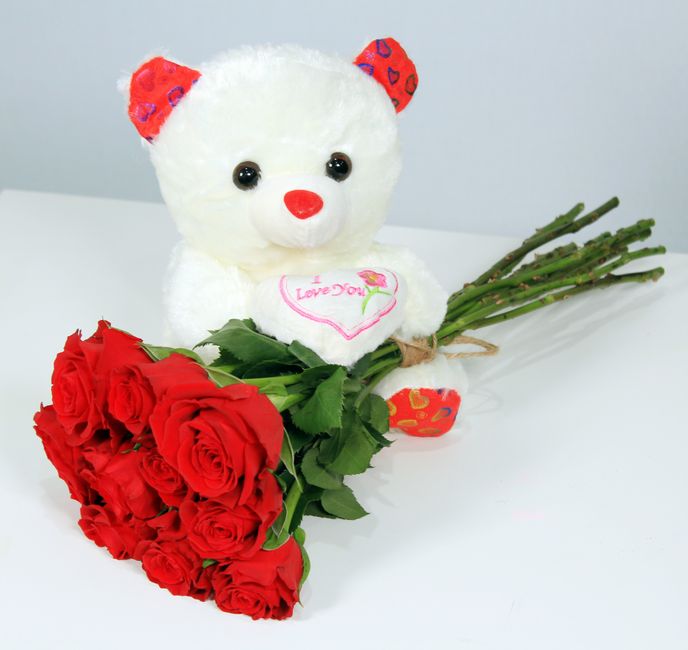 Ours en peluche blanc avec un bouquet de roses rouges et un cœur portant l'inscription "I Love You" sur une table.