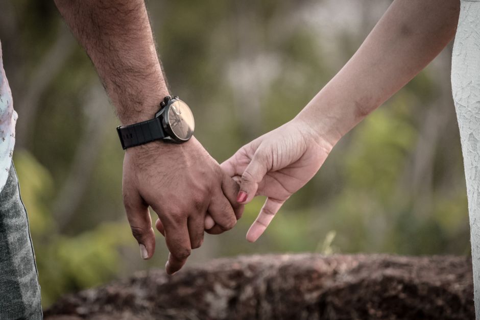 Deux mains se tenant, symbolisant l'amour et la complicité dans un couple, en pleine nature.