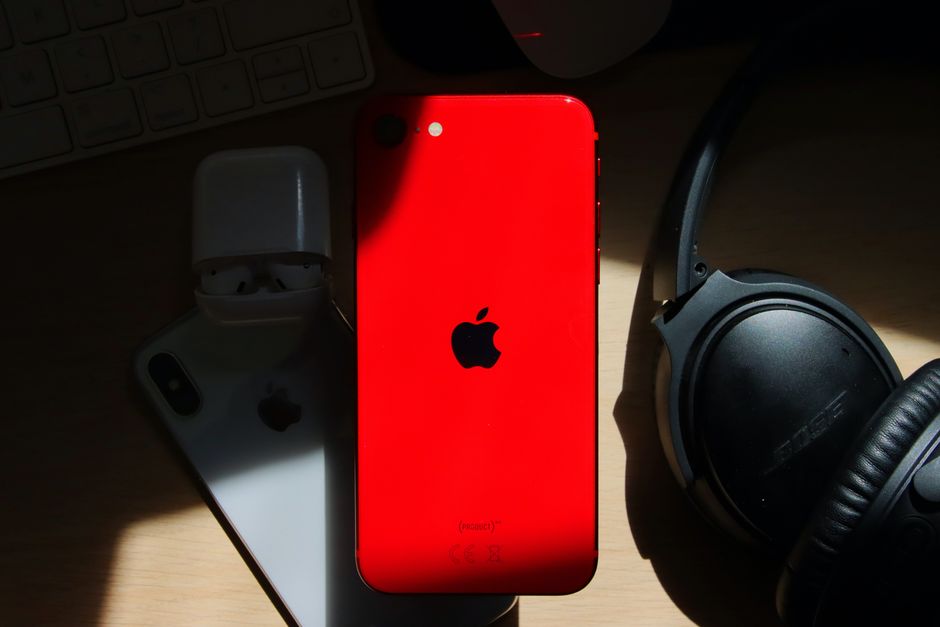 Un smartphone rouge avec le logo Apple, des écouteurs et des AirPods sur un bureau en bois.