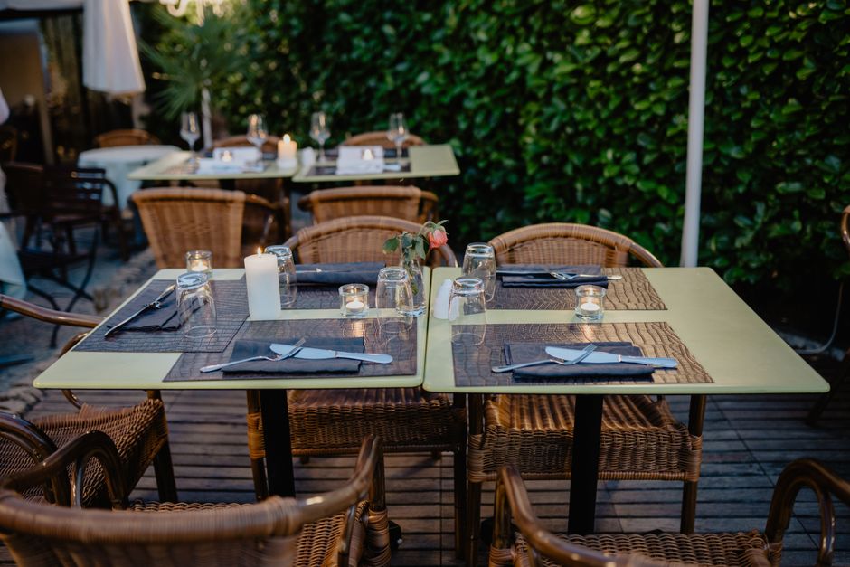 Table élégamment dressée pour un dîner aux chandelles, avec chaises en osier et bougies, entourée de verdure.