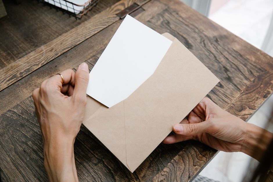 Une personne ouvre une enveloppe en papier kraft sur une table en bois, révélant une carte blanche à l'intérieur.