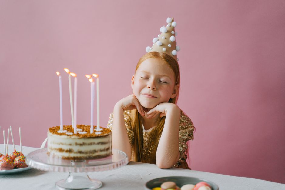 Fille souriante en tenue dorée, devant un gâteau d'anniversaire avec des bougies, décorée d'un chapeau festif.