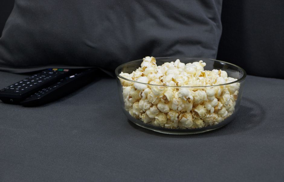 Bol de popcorn sur un canapé gris avec une télécommande à côté, ambiance soirée cinéma chic.