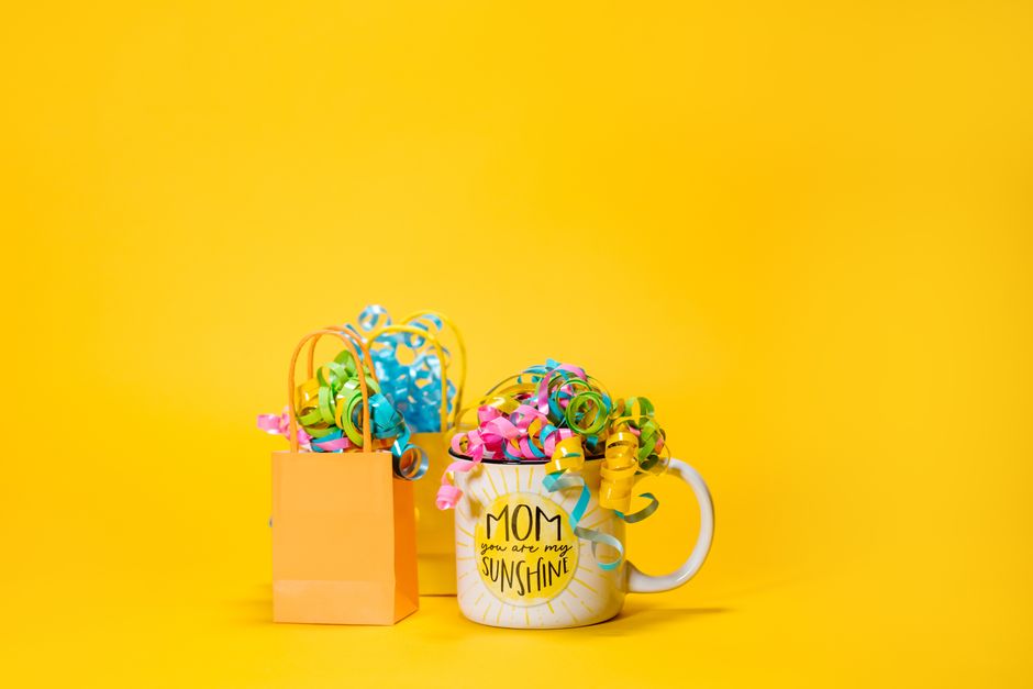 Cadeaux colorés dans une tasse et un sac, sur fond jaune, symbolisant des surprises sans occasion.