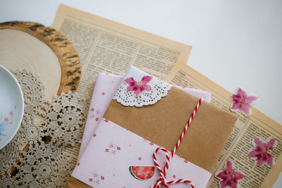 Emballage cadeau minimaliste en papier kraft décoré de fleurs et de dentelle sur un fond de vieux journaux.