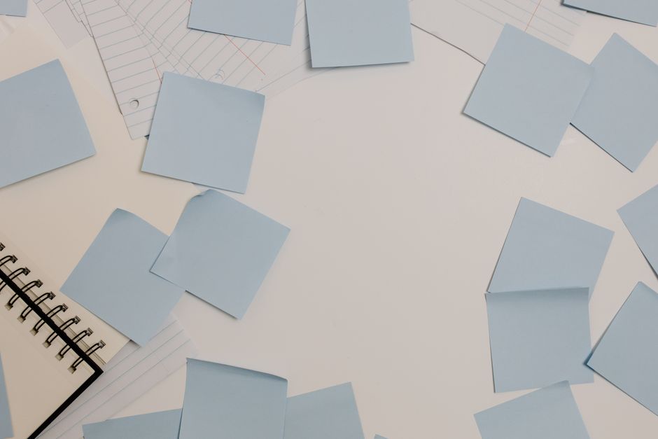 Papier blanc avec des notes autocollantes bleues éparpillées et un carnet à spirale sur le côté, prêt pour une chasse au trés