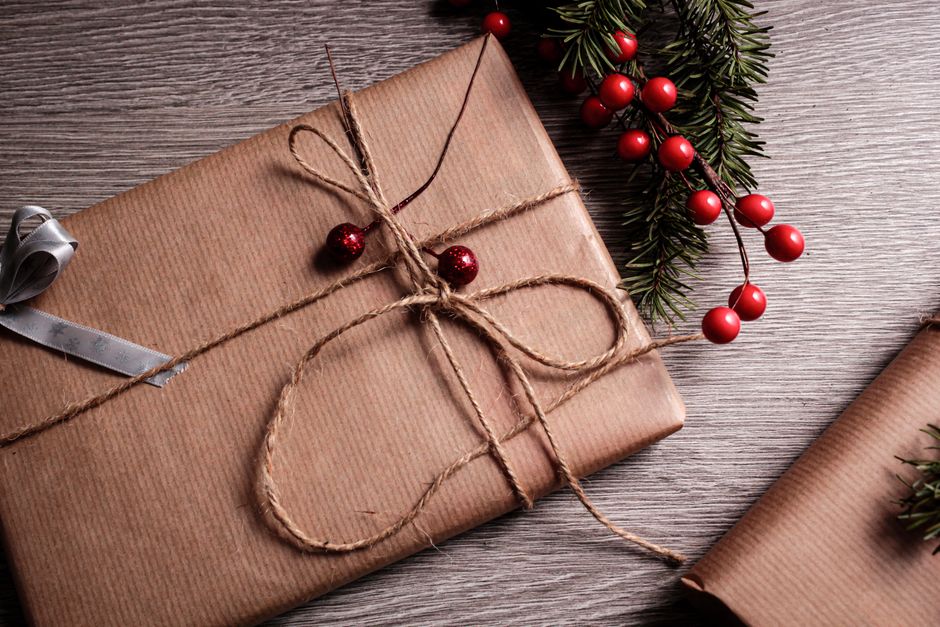 Emballage cadeau en papier kraft avec corde et décorations rouges sur une table en bois.
