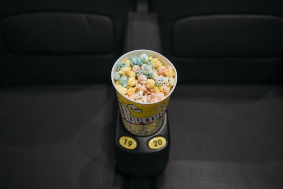 Un seau de popcorn coloré posé sur un accoudoir de fauteuil de cinéma.
