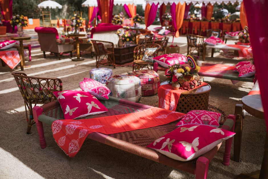 Espace de décoration avec des canapés et coussins roses et rouges, agrémenté de fleurs et de tentures colorées.