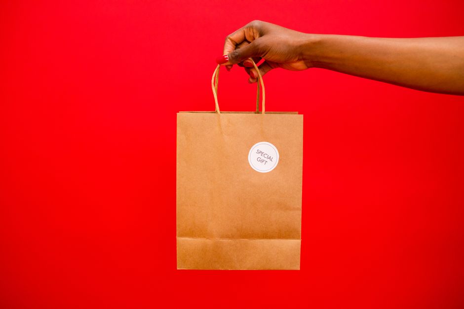 Main tenant un sac cadeau en papier brun avec une étiquette spéciale sur fond rouge vif.