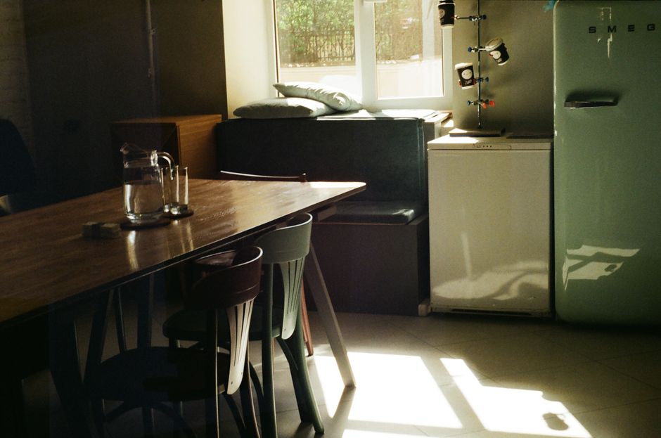 Cuisine moderne avec une table en bois, des chaises colorées et un réfrigérateur Smeg vintage. Lumière naturelle abondante.