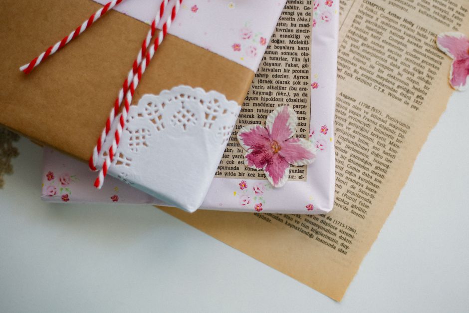 Emballages cadeaux minimalistes en papier kraft et rose, décorés de fleurs séchées et de cordelette rouge.