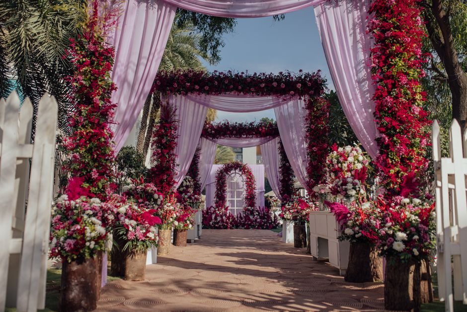 Allée décorée de fleurs roses et rouges avec des drapés en tissu, créant une ambiance élégante et romantique.
