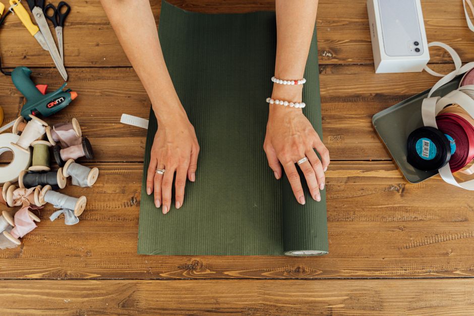 Personne en train d'enrouler du papier cadeau vert sur une table en bois, entourée de fournitures de bricolage.